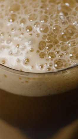 Vertical-Video-Close-Up-Of-Irish-Stout-Being-Poured-Into-Glass-Against-Black-Studio-Background-To-Celebrate-St-Patricks-Day